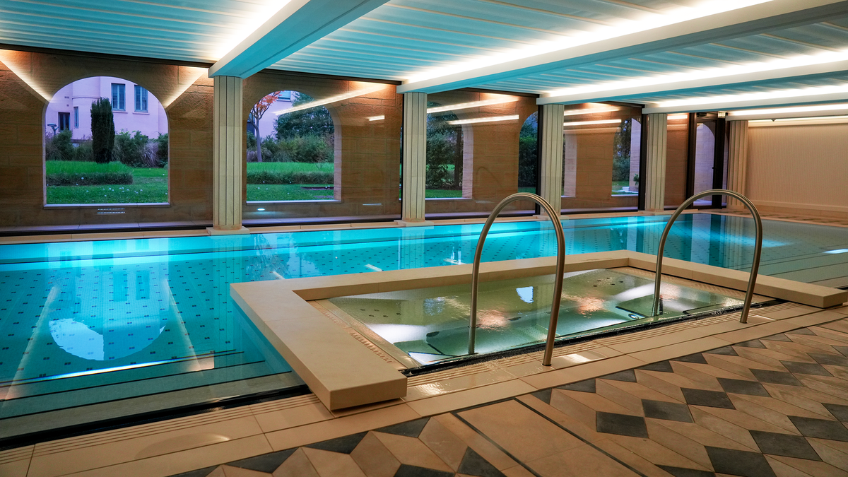 The indoor pool at Villa Maïa, lit turquoise under a ribbed ceiling with garden windows, Lyon