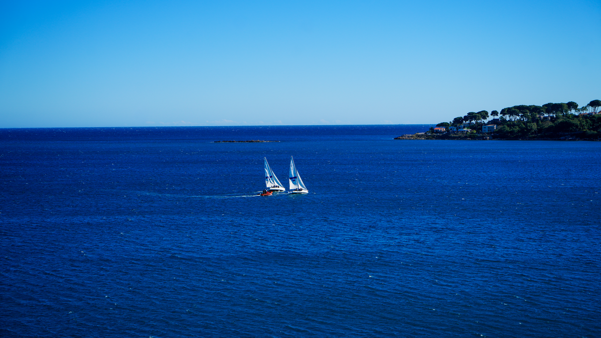 Two sailboats on the deep blue Mediterranean off the pine-topped Cap d'Antibes, French Riviera