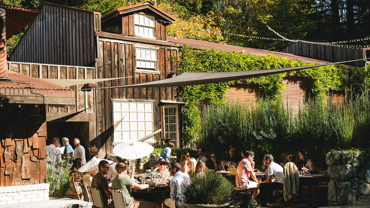 Guests dining outdoors under shade sails beside the weathered redwood barn at Big Sur Food & Wine