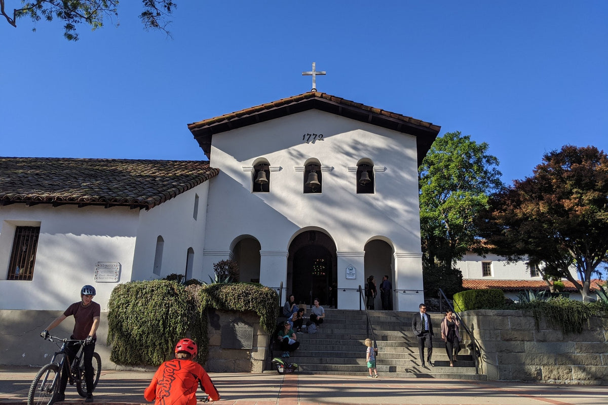 The white bell-tower façade of Mission San Luis Obispo de Tolosa with cyclists passing on a sunny day